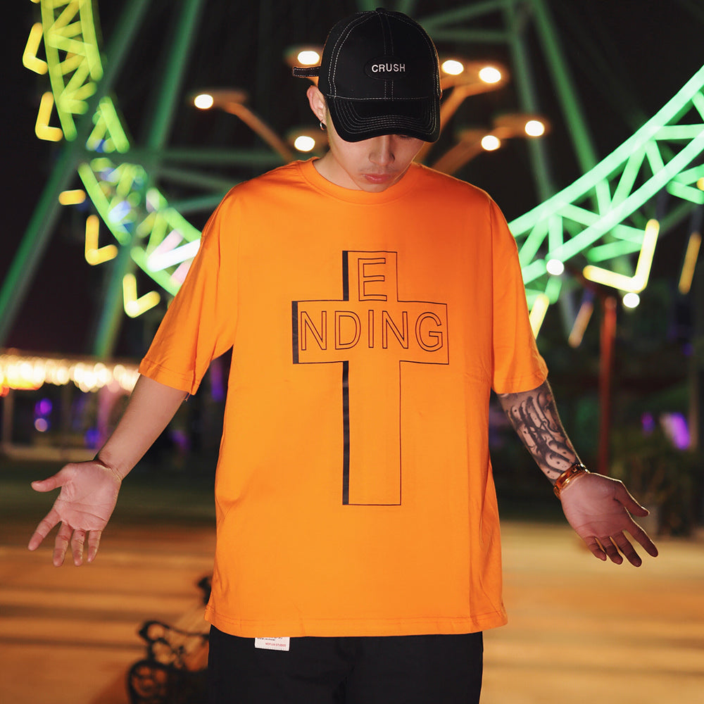 Person wearing an orange t-shirt with a black cross design and 'ENDING' text, standing in front of colorful neon lights.