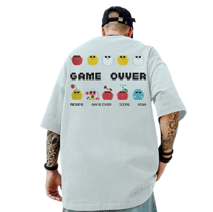 Person wearing a white t-shirt with a retro game design on the back, standing against a blue sky and rocky landscape.