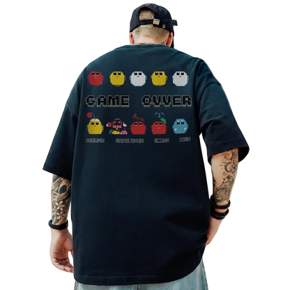 Person wearing a black t-shirt with a retro game design, standing outdoors with a blue sky and clouds in the background.