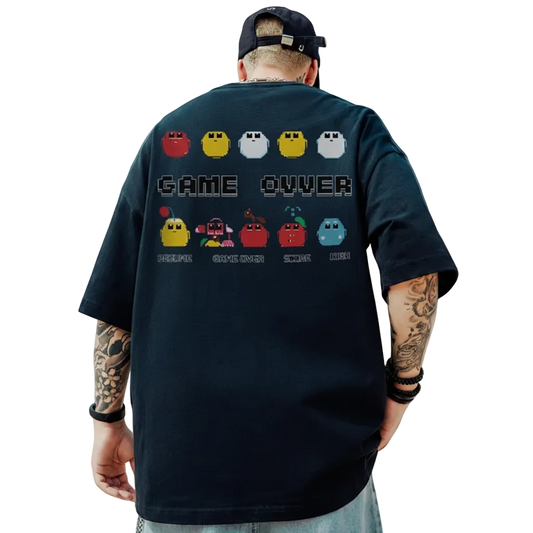 Person wearing a black t-shirt with a retro game design, standing outdoors with a blue sky and clouds in the background.