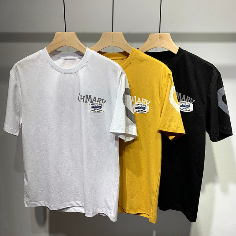 Three t-shirts in white, yellow, and black hanging on a rack with a brand logo.