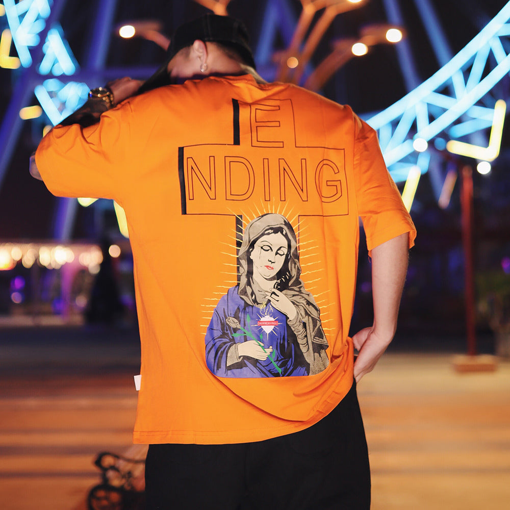 Person wearing an orange t-shirt with a graphic design and text, standing in front of colorful lights.